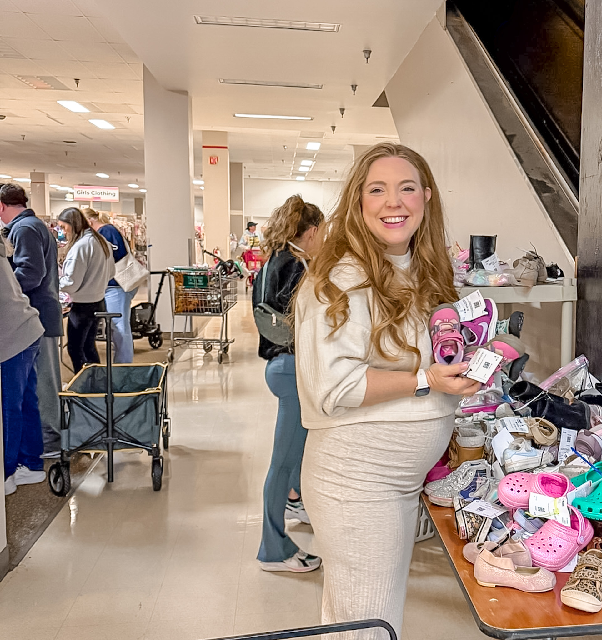 Woman shopping the shoes area and holding a pair of shoes she found for her child. She's smiling and showing off the shoes.