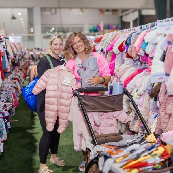 two smiling women standing between two racks of girls' clothing