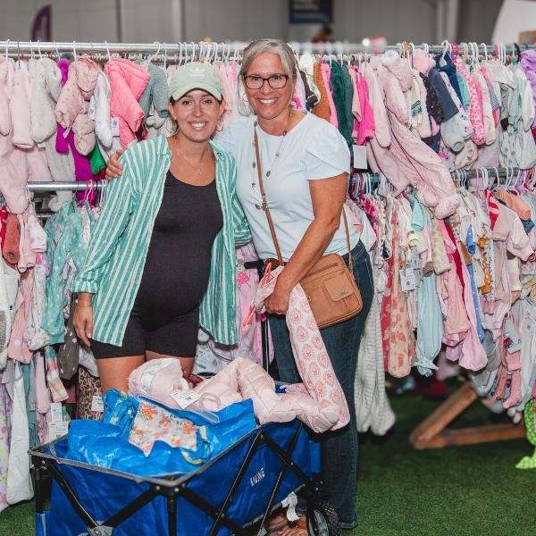 two smiling women shopping for girls' clothing with a wagon