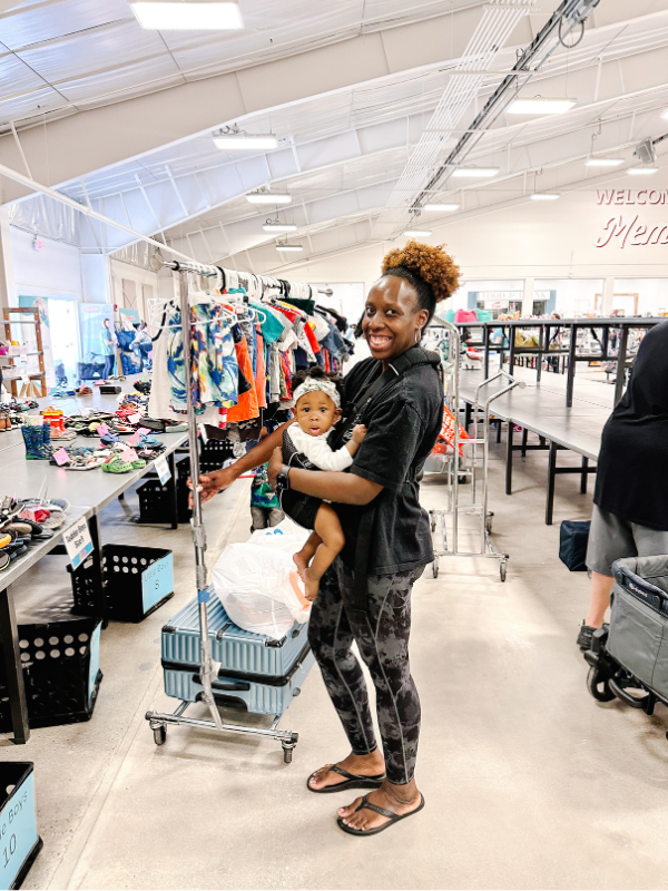 Baby wearing Mom using clothign rolling rack to drop off items at the JBF Harrington Children's consignment sale
