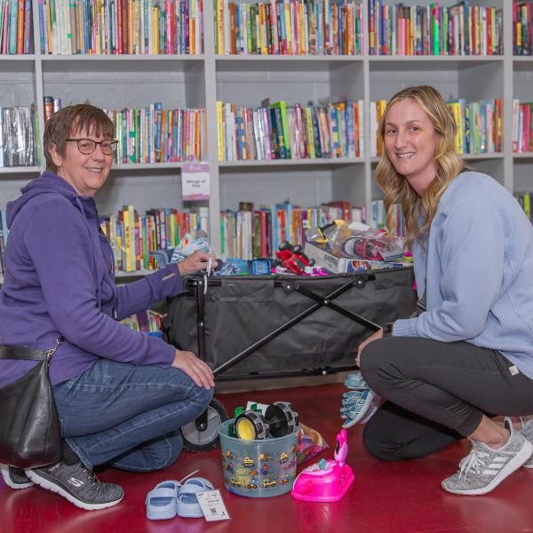 two smiling women kneeling on the ground looking at shelves of books
