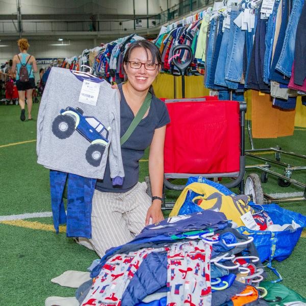 smiling woman kneeling on the ground with a pile of boys' clothing